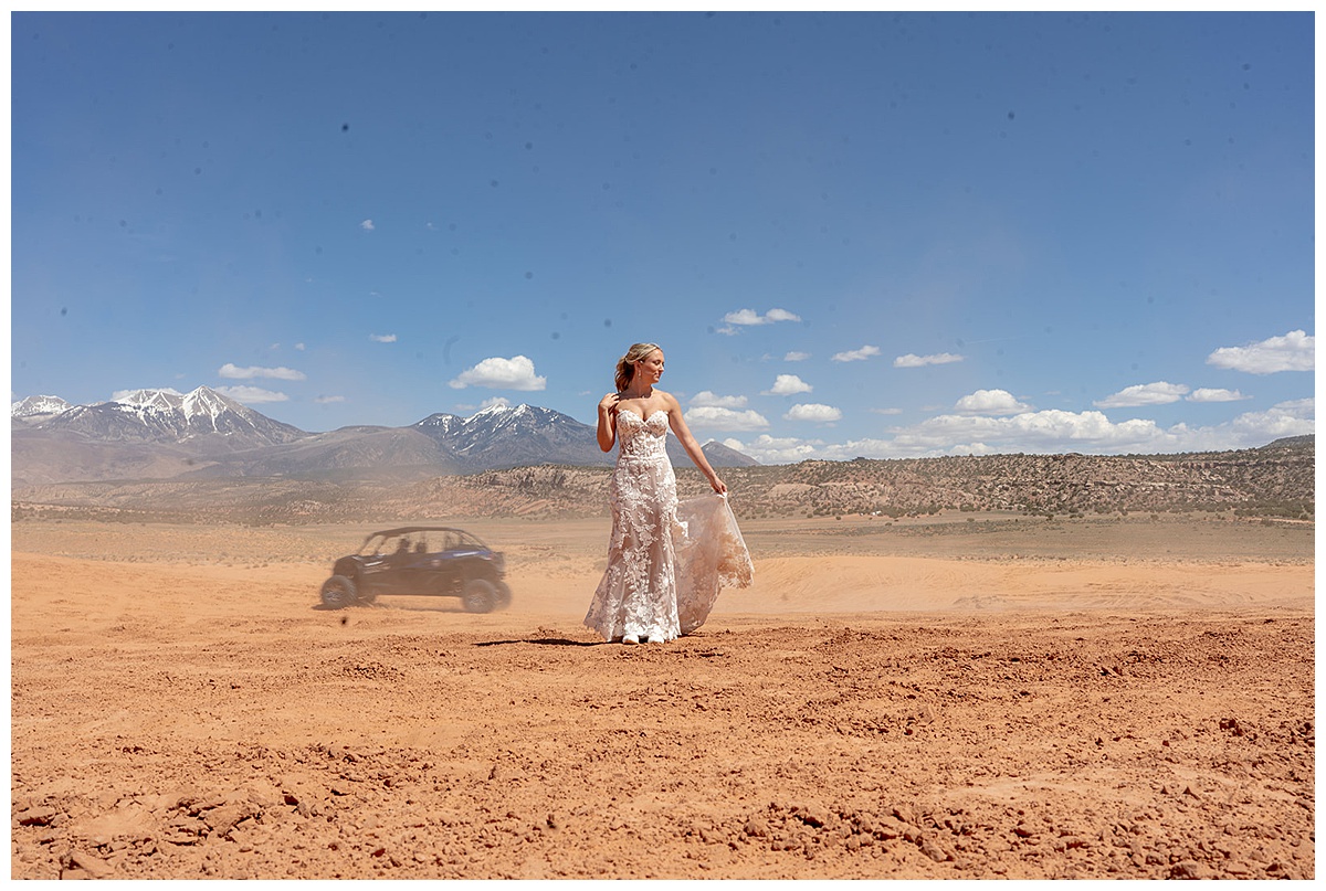 A bride in the desert with an ATV behind her creating dust