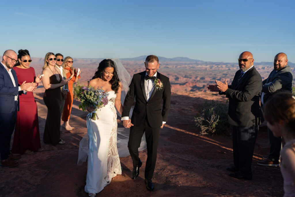 Bride and groom leaving their ceremony on top of the cliffs overlooking canyons at moab utah
