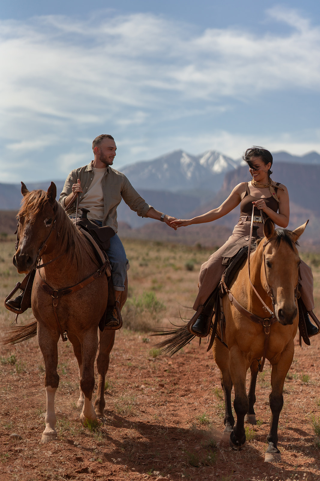 Close-up of elopement couple on horseback, holding hands and smiling as they ride forward.