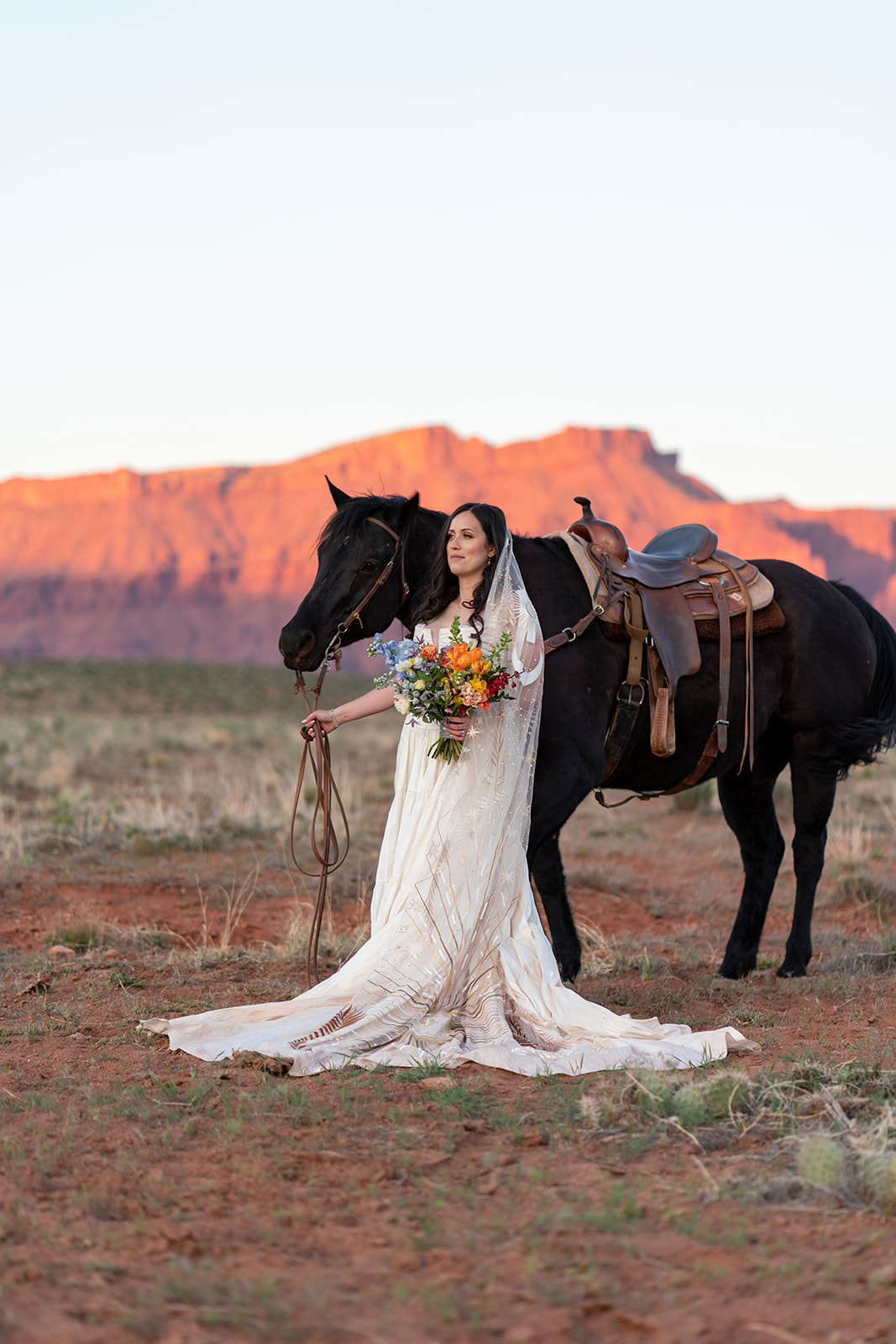 The sunset light illuminates the massive red rock cliffs in the background. Moab Western-style elopement.