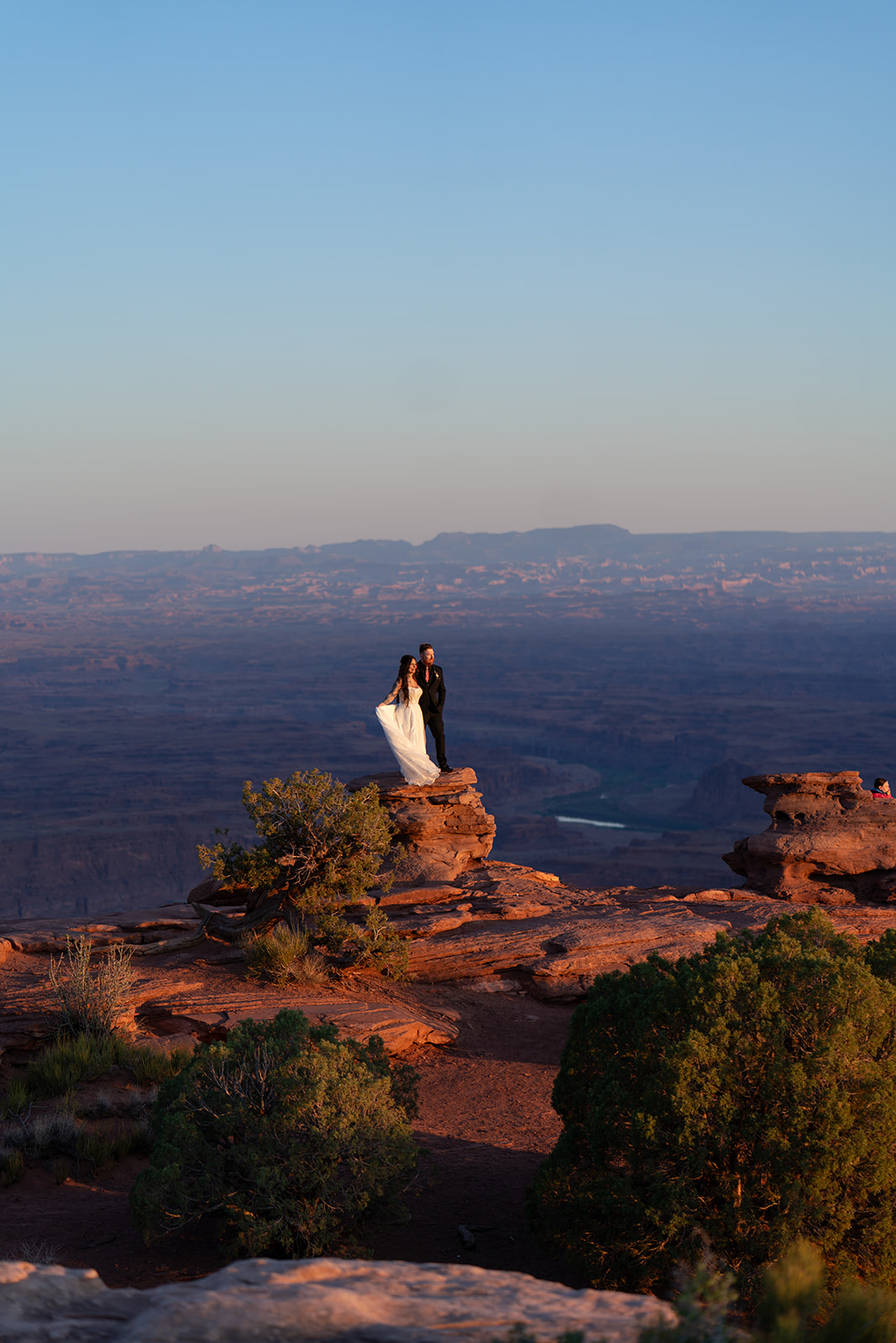 A wide shot of a couple on a cliff during a stunning sunset in Utah