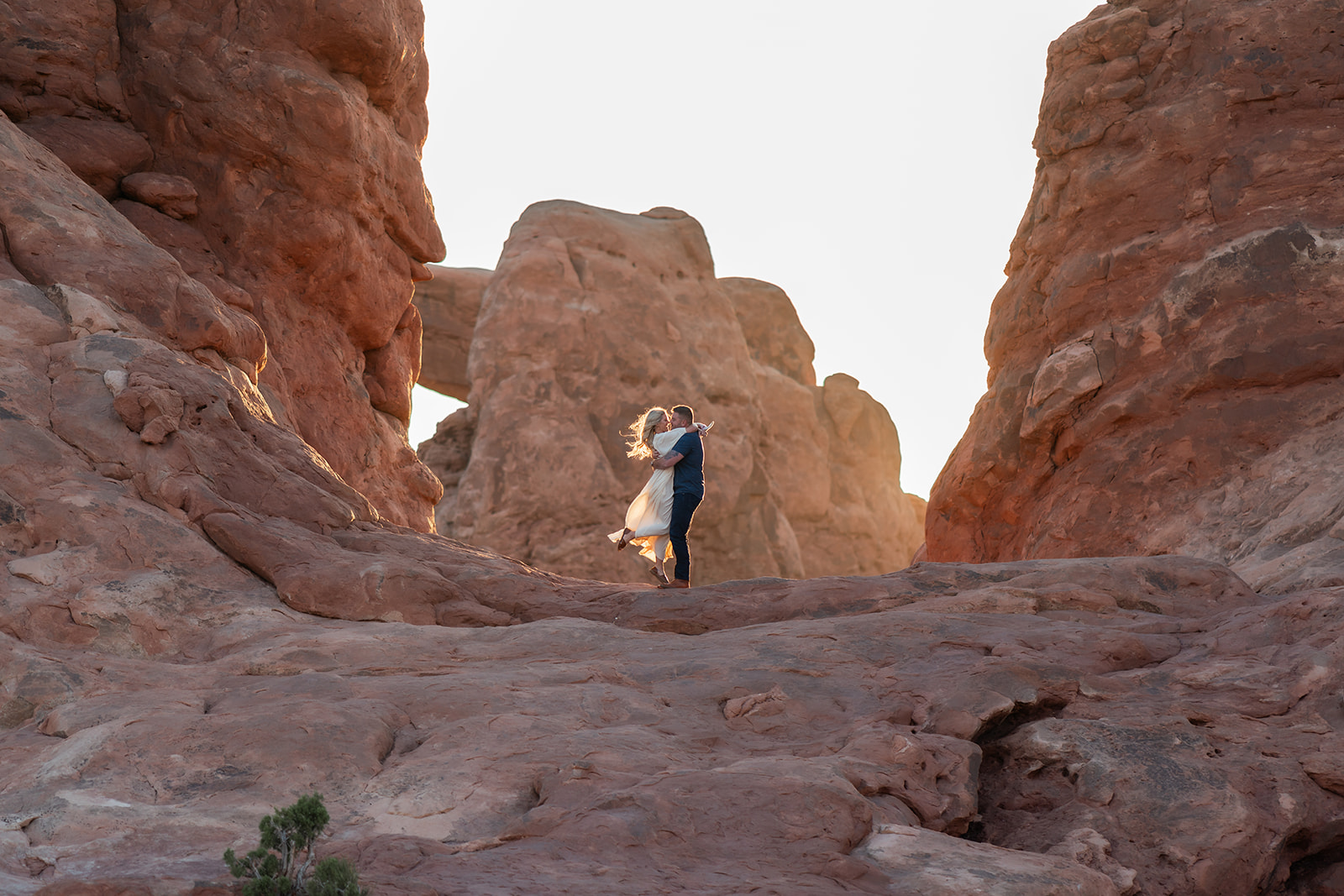 A long shot of a couple on a cliff overlooking the vast desert landscape of Utah