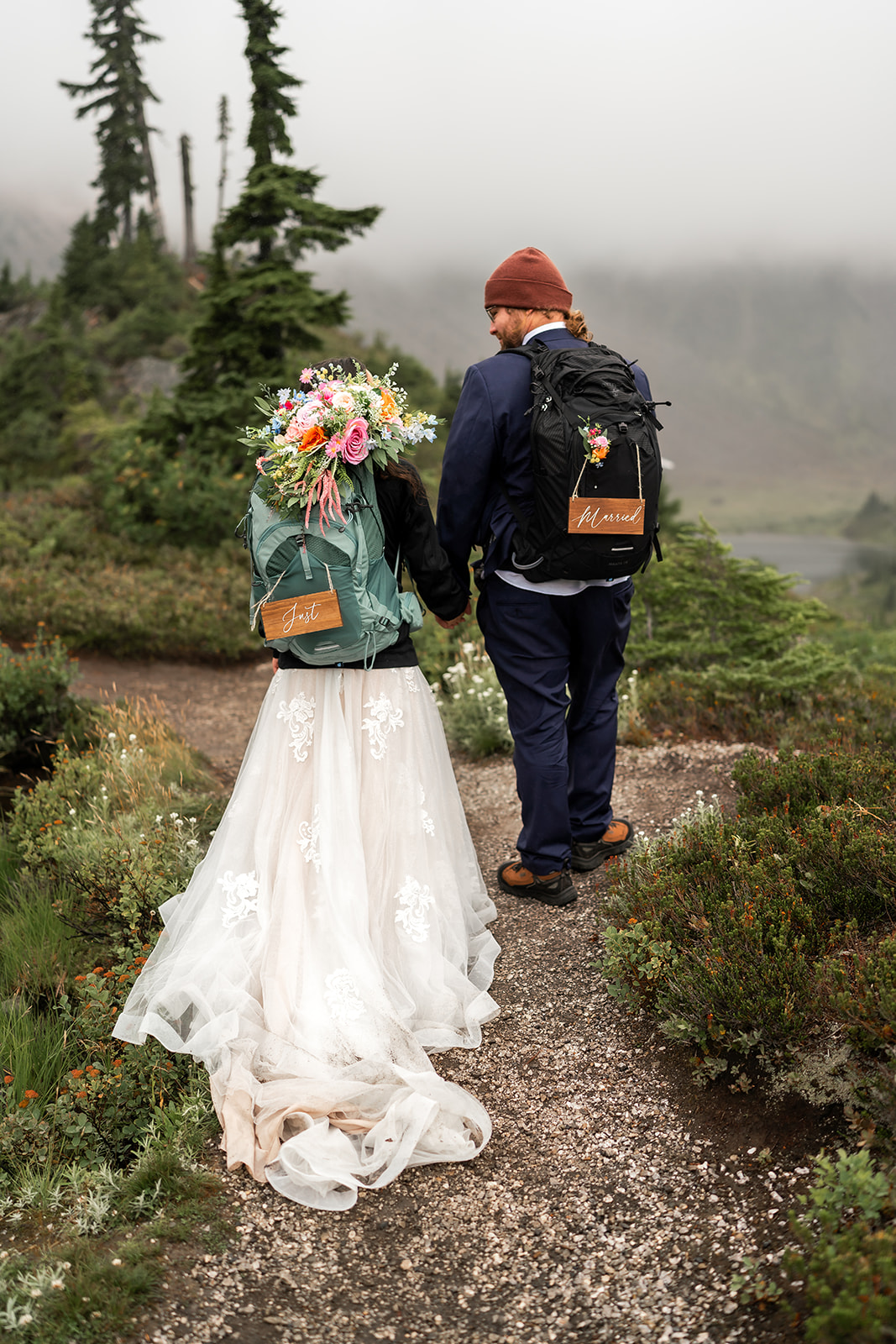 A newly married couple walks away from the camera on a foggy trail
