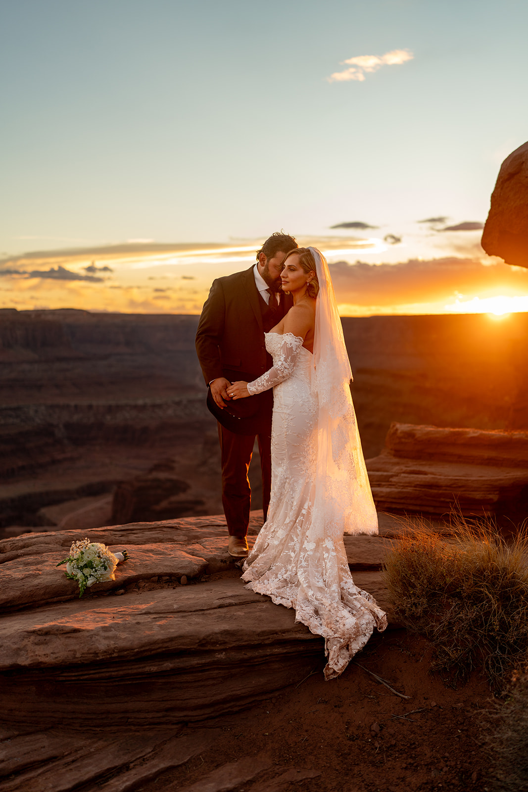 A newly wed couple embracing on a cliff edge at sunset-Wedding in Utah