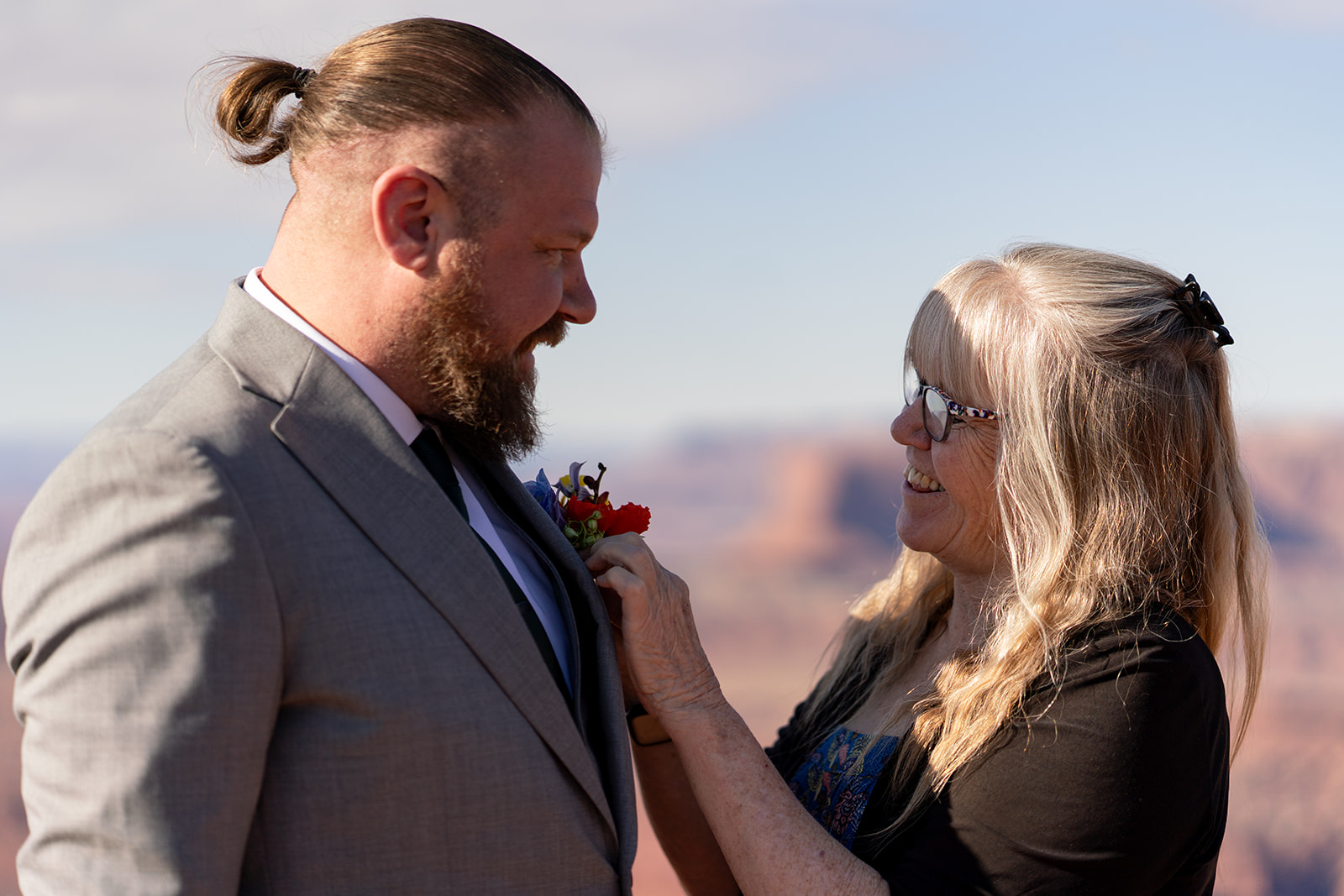 Candid photo of the groom receiving his boutonniere, featuring red and blue desert blooms, created by Tangled Sage Event Artistry, before his Moab wedding