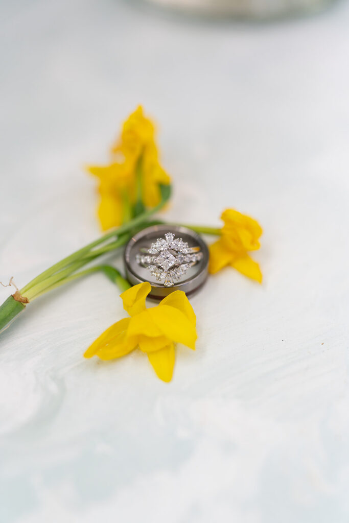 Detail shot of diamond and silver wedding rings styled with a yellow daffodil, capturing the fine details of a Moab wedding