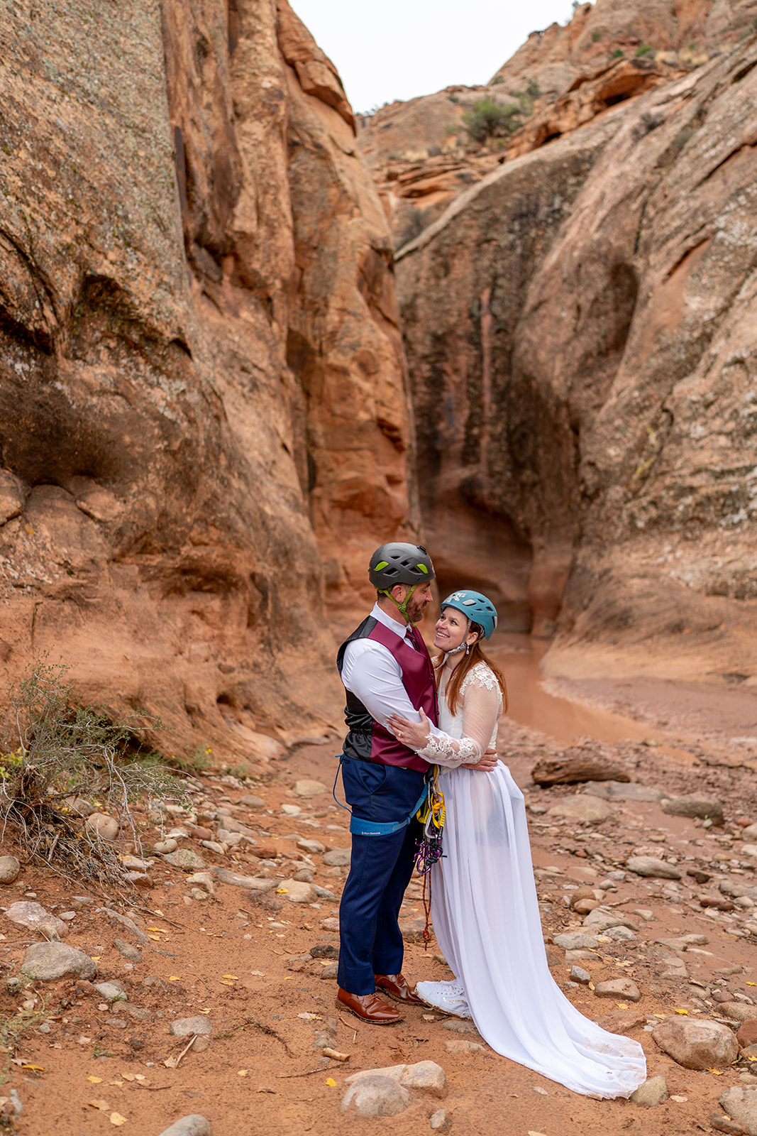 Couple in wedding attire and climbing gear embrace in a rocky canyon in Moab, Utah
