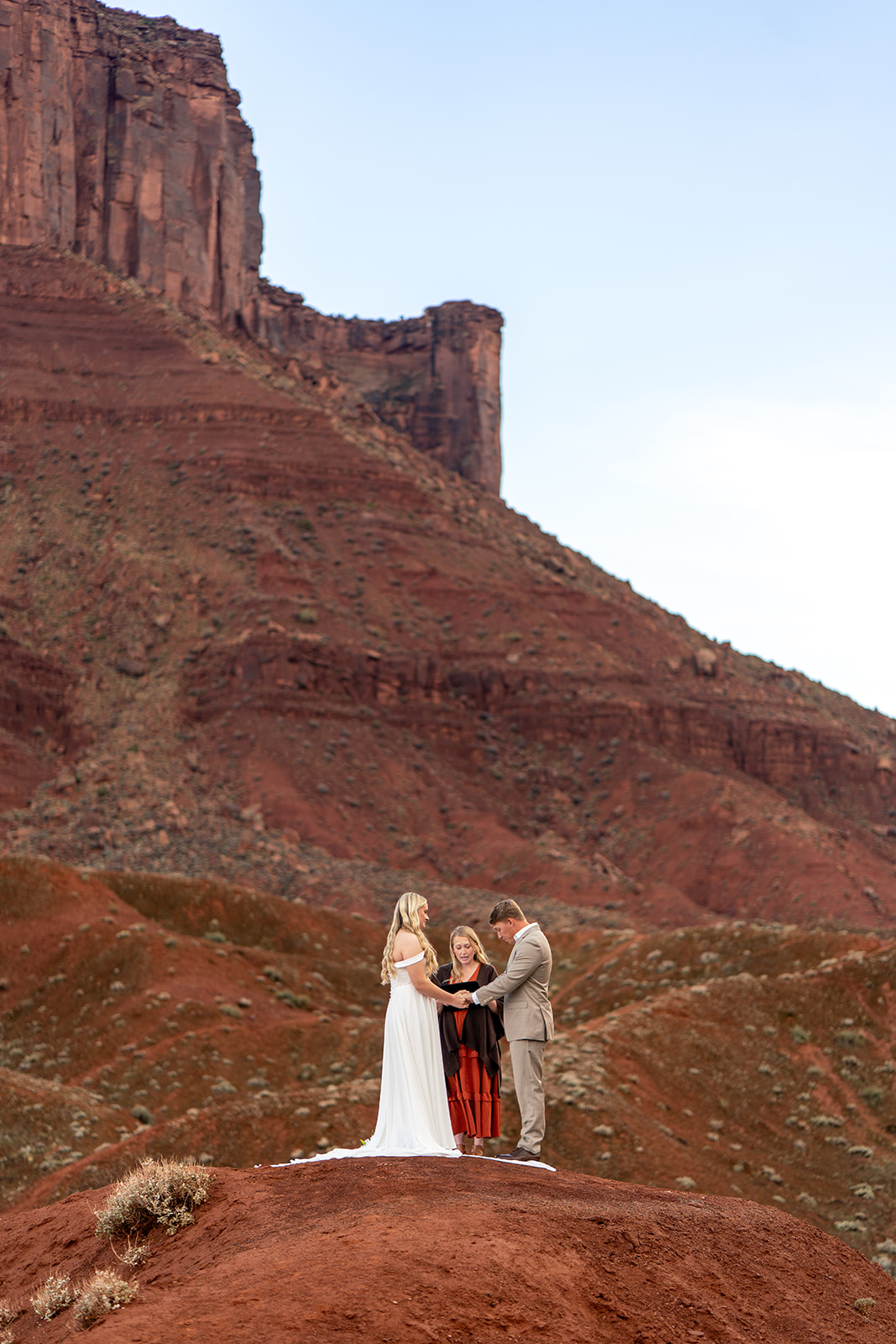 Bride, groom, and officiant holding an intimate elopement ceremony on a red rock hill in Moab, Utah, providing a visual guide for finding elopement officiants and outdoor wedding venues